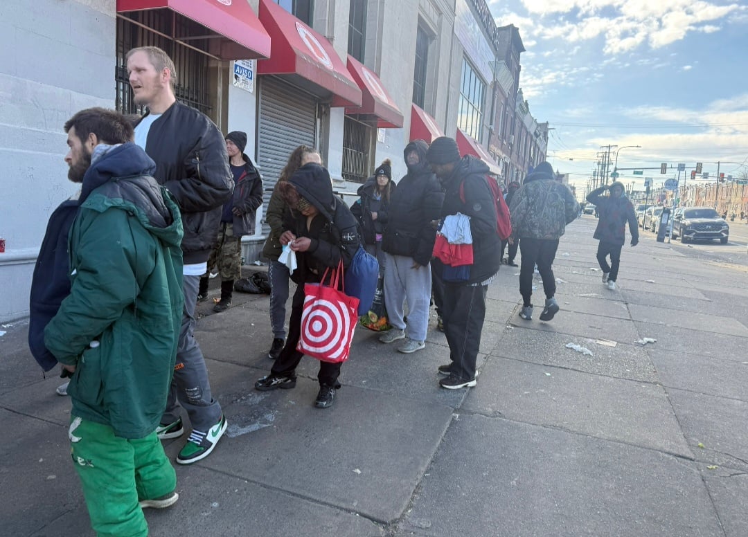 Group of people standing in line on a city street during daytime with buildings and urban landscape visible