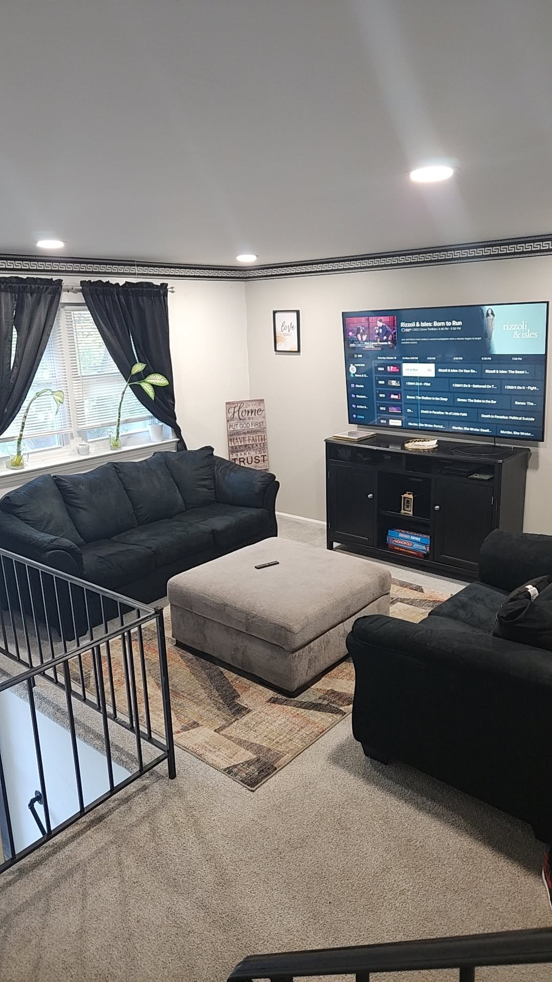 Modern living room with black furniture, TV on entertainment center, infant crib, and large window with dark curtains